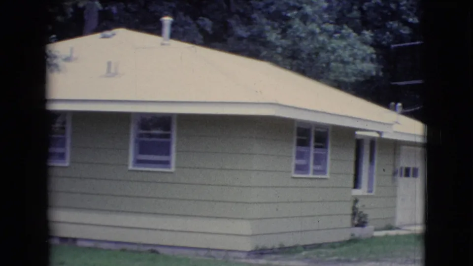 1961 Clarkdale frame focused on a yellow-sided house with sloped roof, windows, garage edge, roof vents, trees, and antenna.