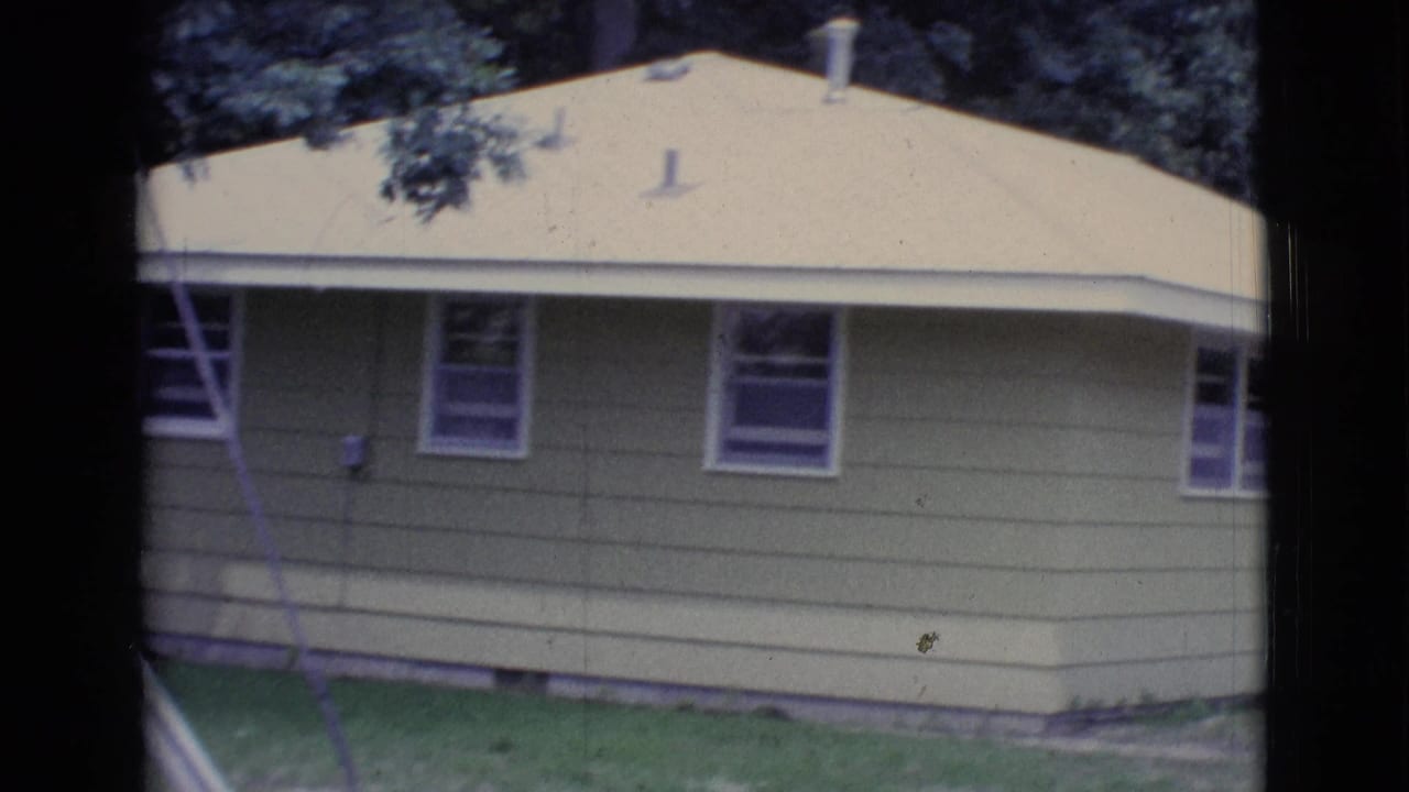 Light-colored house with pale roof, windows, lawn, trees, and a diagonal white pole at the edge.