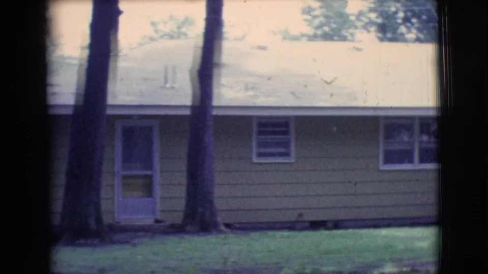 1961 Clarkdale, Arizona frame showing the front or side of a yellow house with a door, windows, trees, and grass.