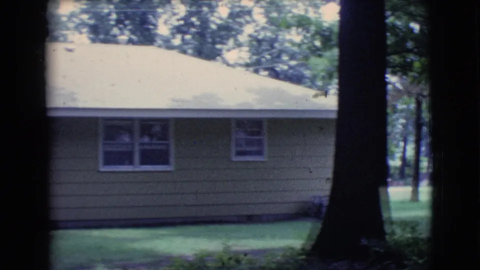 1961 Clarkdale, Arizona home-movie frame of a yellow house exterior, framed by trees with windows and lawn visible.