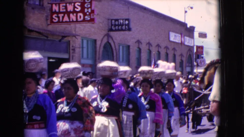 A closer 8mm view shows the parade group in colorful attire, silver necklaces, and head-carried baskets on a Clarkdale street in 1961.