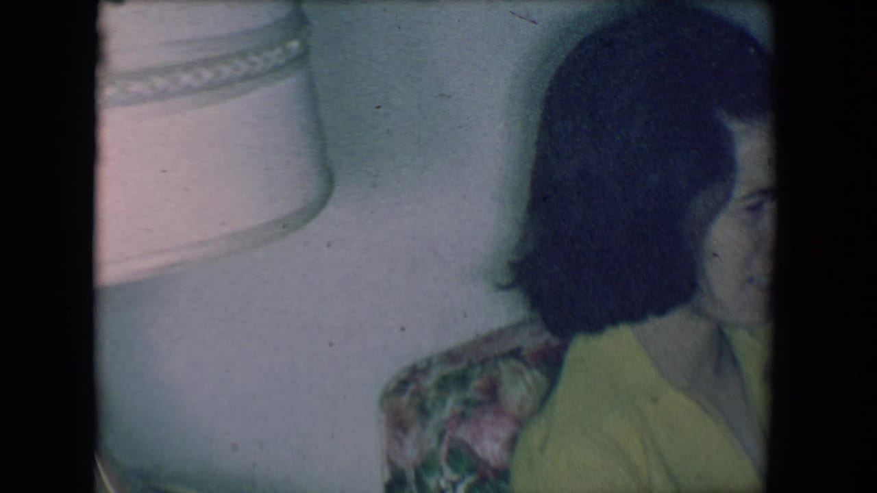 Woman in yellow seated beside a light-colored lamp on a floral couch.