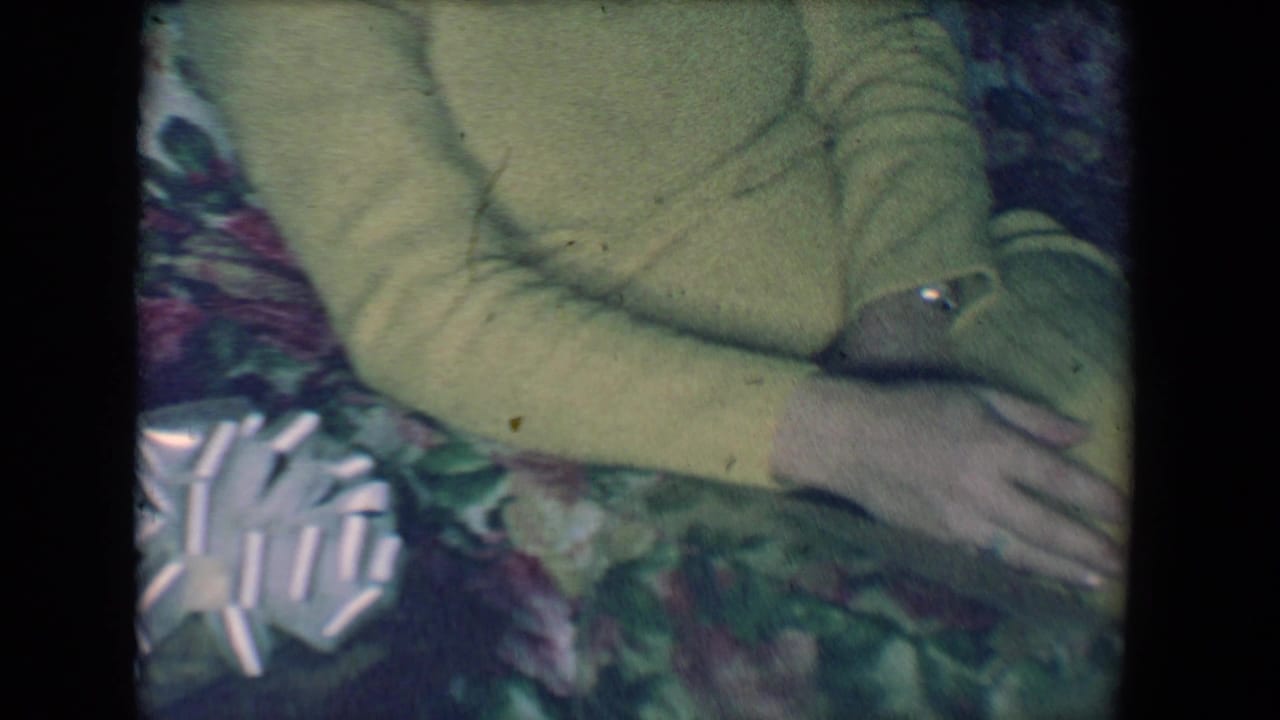 Folded hands and yellow sleeves above floral couch fabric with a white bow-like object nearby.