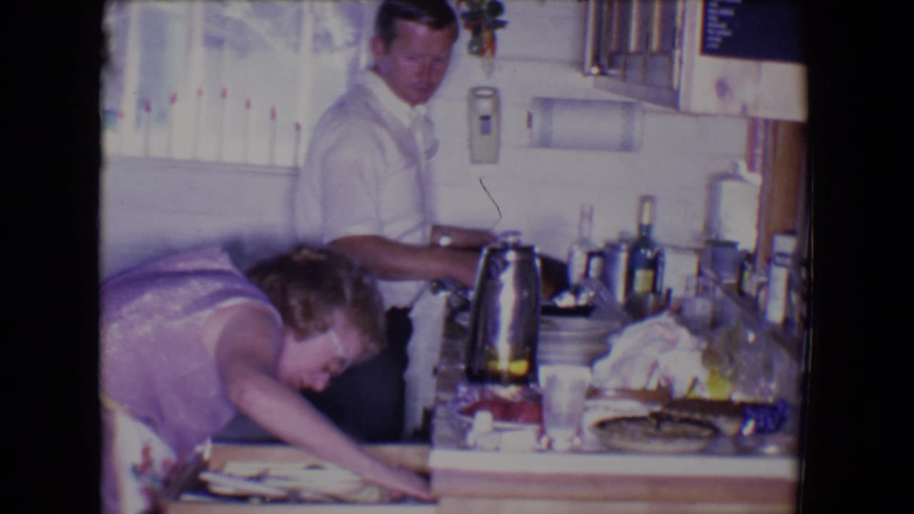 The woman leans deeply into the drawer area while the man remains near the counter in the 1961 Salton Sea kitchen scene.