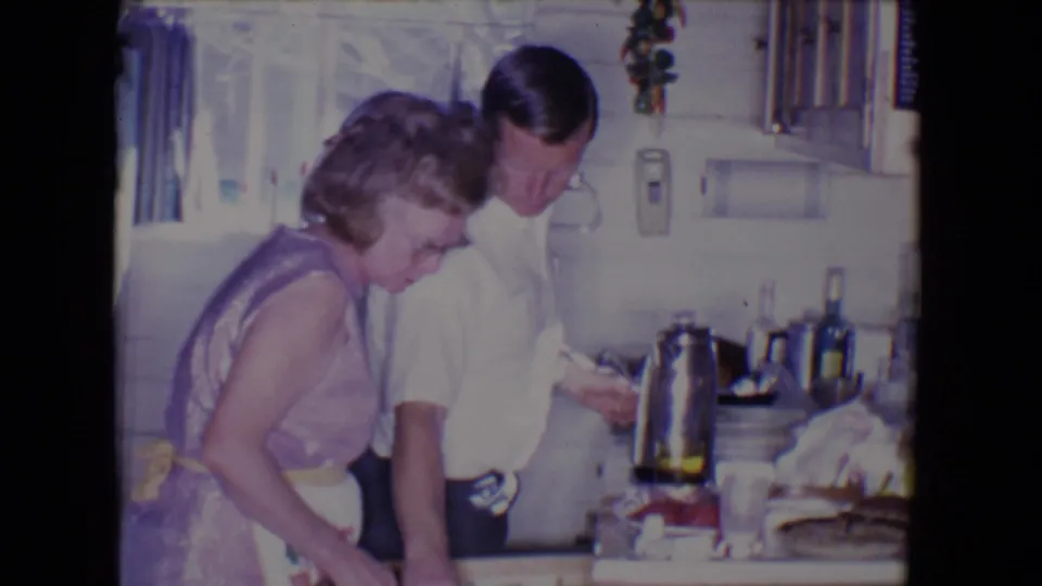 In the 1961 Salton Sea kitchen, the woman and man lean near the counter as household items fill the foreground.