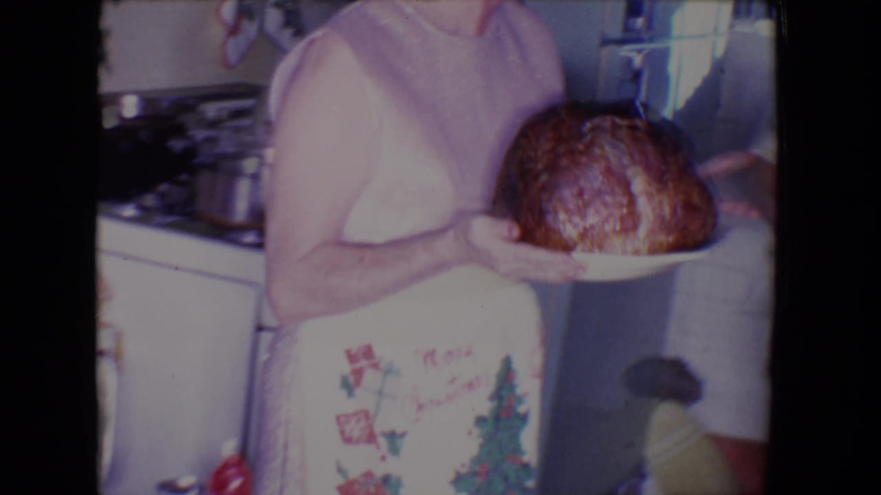 In 1961 Salton Sea home-movie footage, a woman in a holiday apron presents a roasted turkey inside a private kitchen.