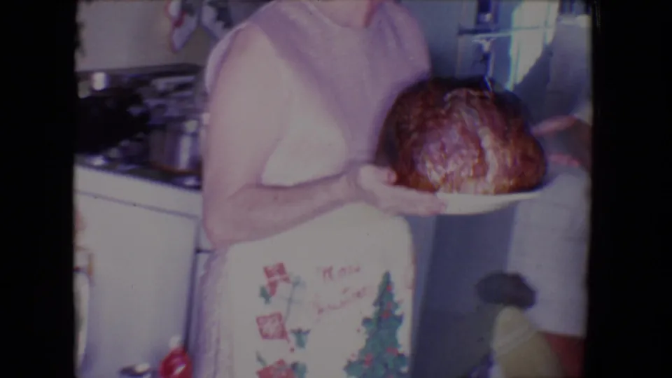 In 1961 Salton Sea home-movie footage, a woman in a holiday apron presents a roasted turkey inside a private kitchen.