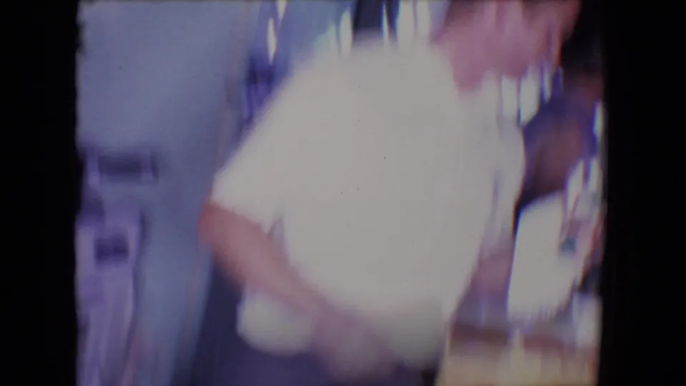 A man in a white shirt appears briefly and out of focus during the 1961 private kitchen home-movie scene.