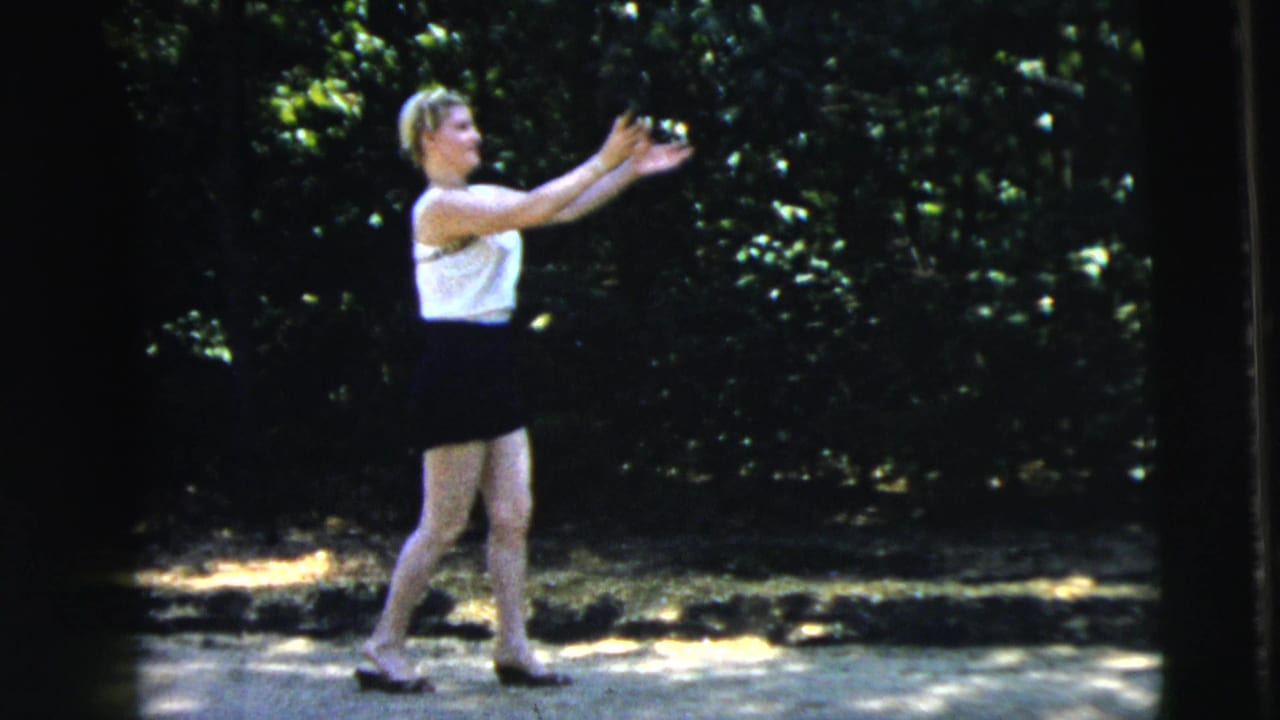Young woman in a white top and dark skirt reaches for a small ball outdoors.