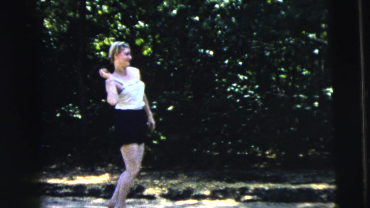 Teenage girl in a white top and dark skirt stands on a sun-dappled road near trees.
