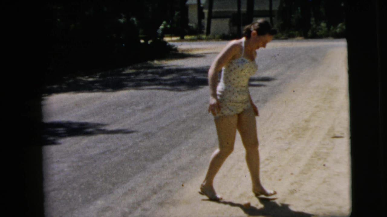 The woman stands on the sunlit roadside in Camden, New Jersey, looking down at the small ball near her feet.