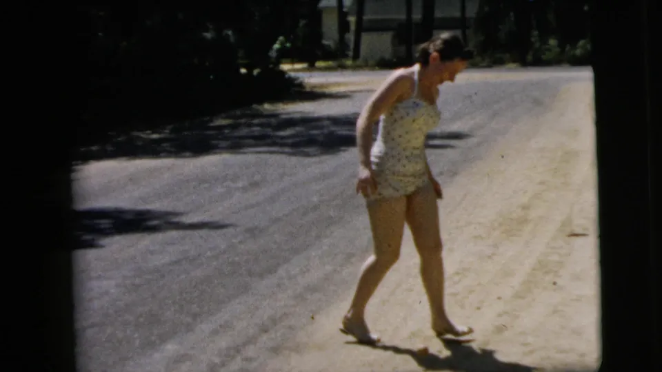 The woman stands on the sunlit roadside in Camden, New Jersey, looking down at the small ball near her feet.