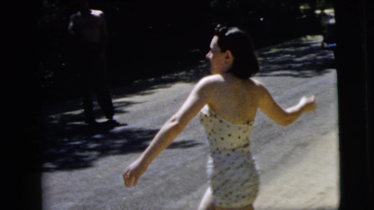 Young woman in a polka-dot swimsuit seen from behind on a shaded road.