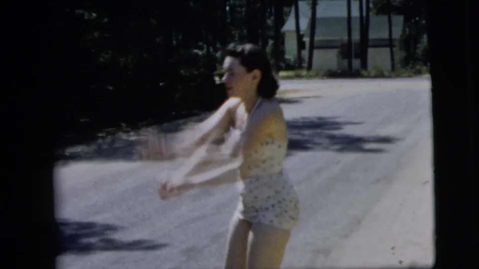 In a 1962 Camden street scene, the young woman turns toward the camera with arms extended, suggesting the moment of tossing or catching an object.
