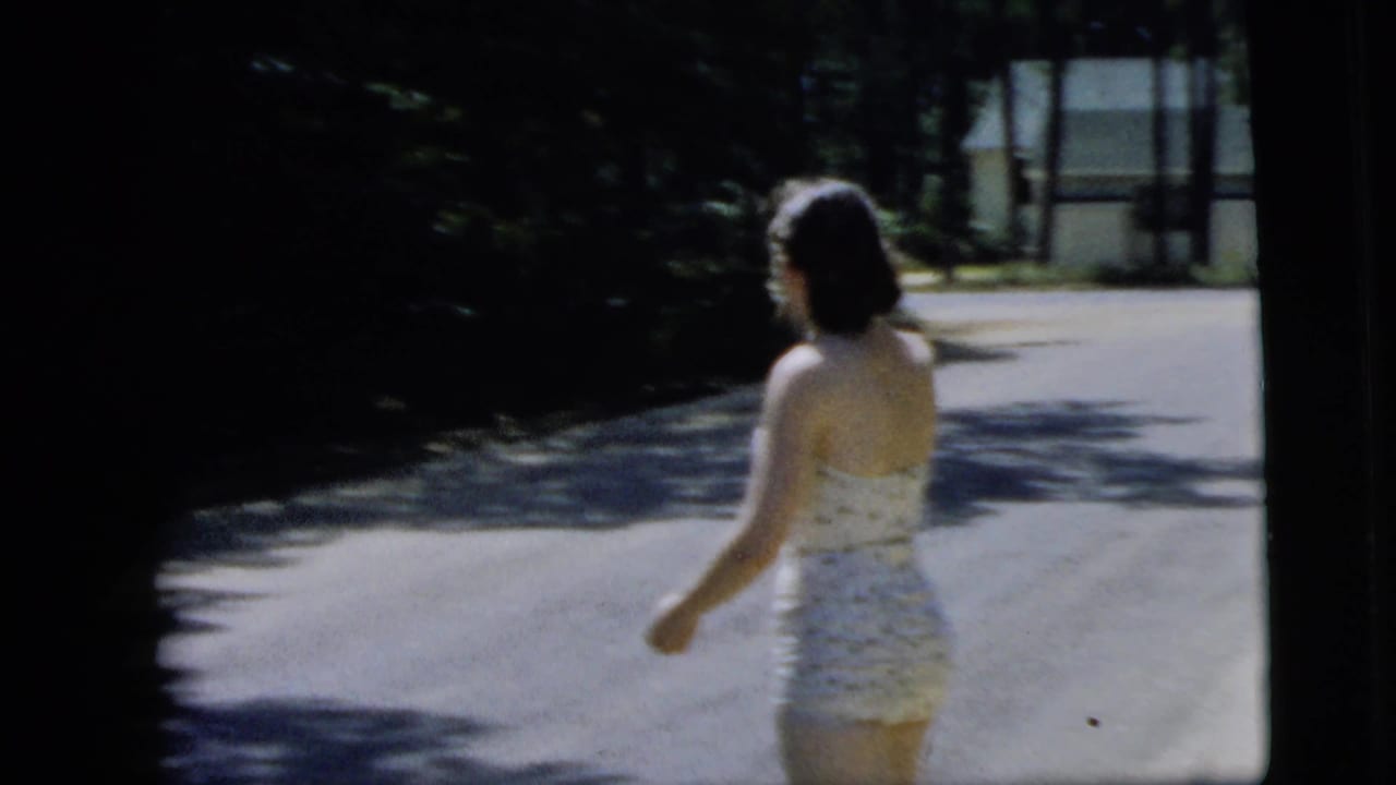 Woman in a white polka-dot swimsuit walking on a sunlit street.