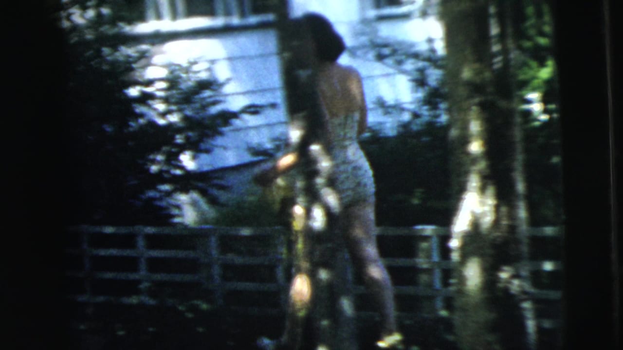 In 1962 Camden, New Jersey footage, a woman in a light patterned dress walks away from the camera through a shaded residential yard.