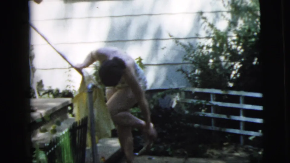 The woman bends near the porch tap area in the residential yard, apparently rinsing or washing her feet beside the steps.