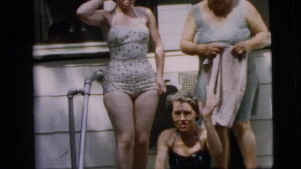 Three women in summer swimwear gather on porch steps in Camden, New Jersey, with one crutch visible beside the standing woman.