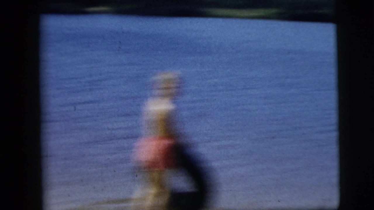 Blurred person in red near water or pavement, framed by dark film edges.