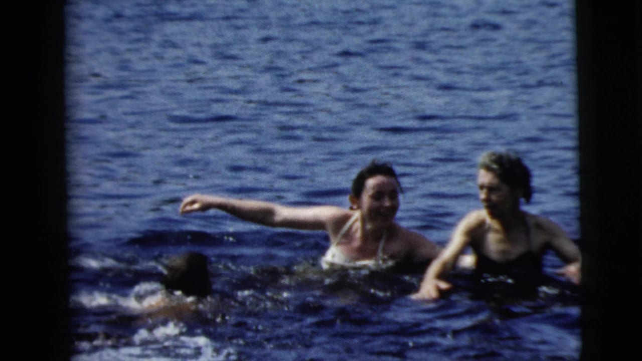 Two women stand in dark blue water while another swimmer splashes nearby.