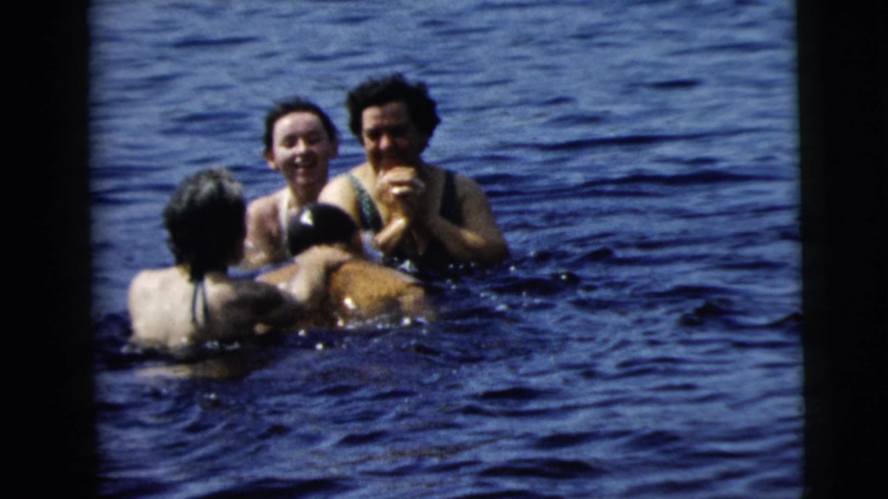 Four swimmers cluster together in open water, smiling and facing one another.