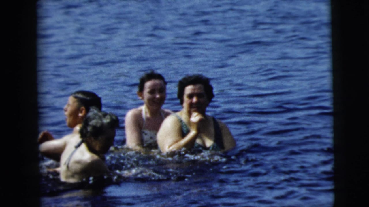 Women in swimsuits smile and tread water in open blue water.