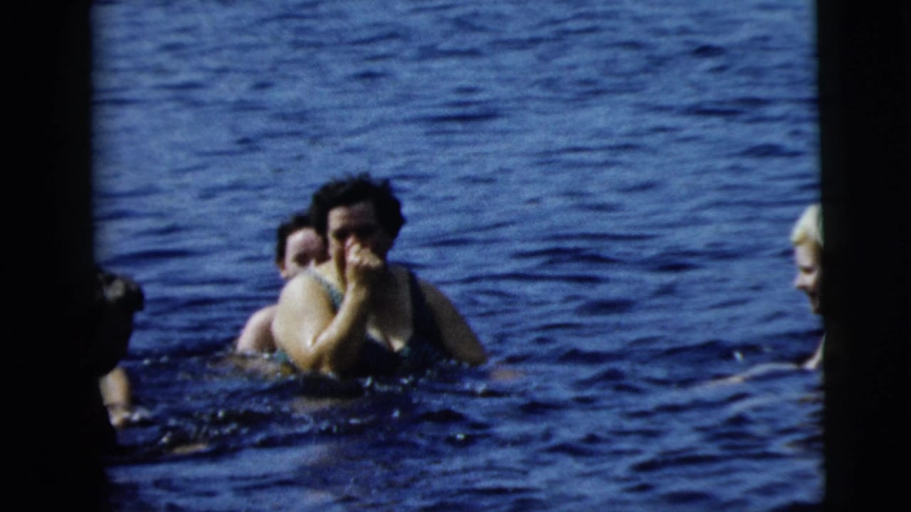 Two women in swimsuits look toward the home-movie camera while treading water, with another swimmer partly visible at the edge of the frame.