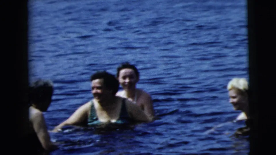 1962 8mm home-movie frame from Camden metadata showing swimmers in a lake, including women in swimsuits and a younger blond swimmer.