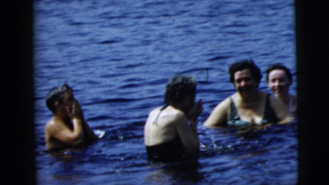 Camden, New Jersey 1962 home-movie frame showing swimmers conversing in lake water, with one person wiping water from their face.