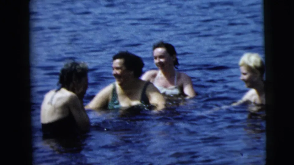 1960s 8mm frame showing a small group of lake swimmers in Camden metadata, with women and a younger blond swimmer gathered together.