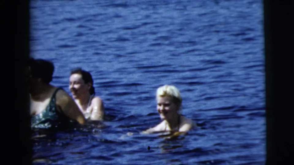 Camden 1962 8mm home-movie frame with swimmers partially submerged in a lake, including a younger blond swimmer facing the camera.