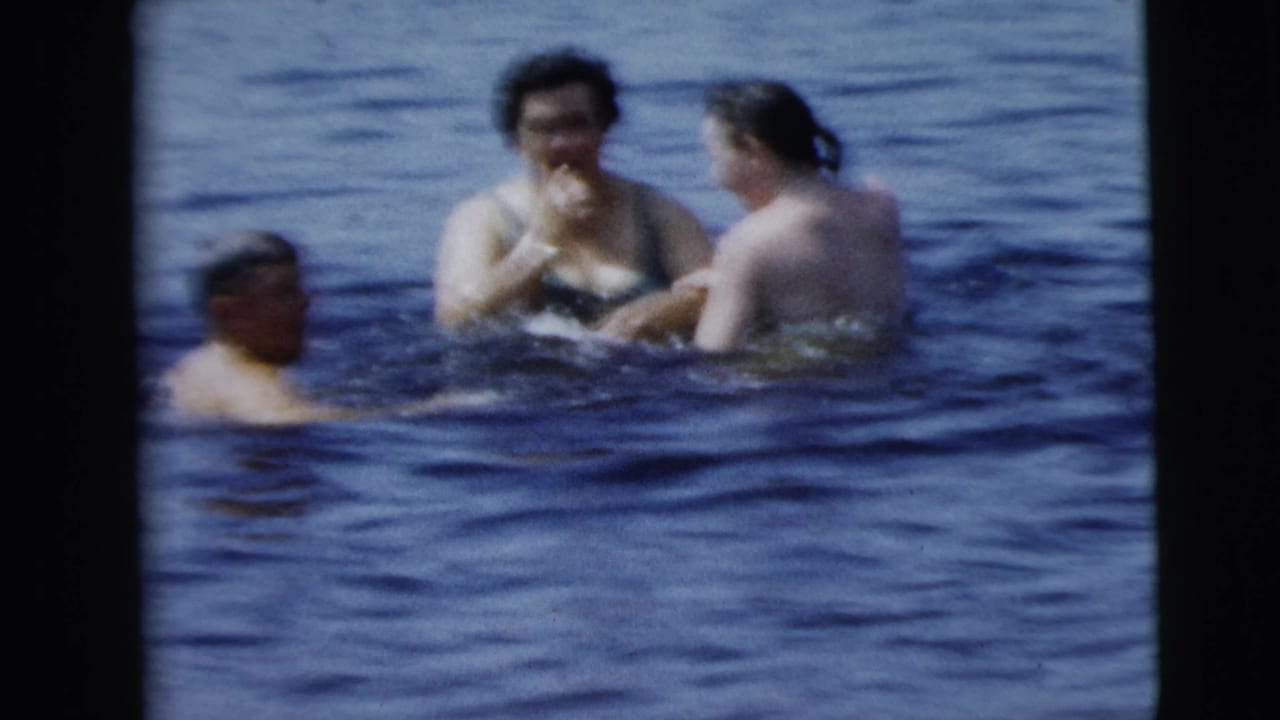 1962 8mm home-movie frame from Camden, New Jersey, showing three adults wading close together in rippled open water.