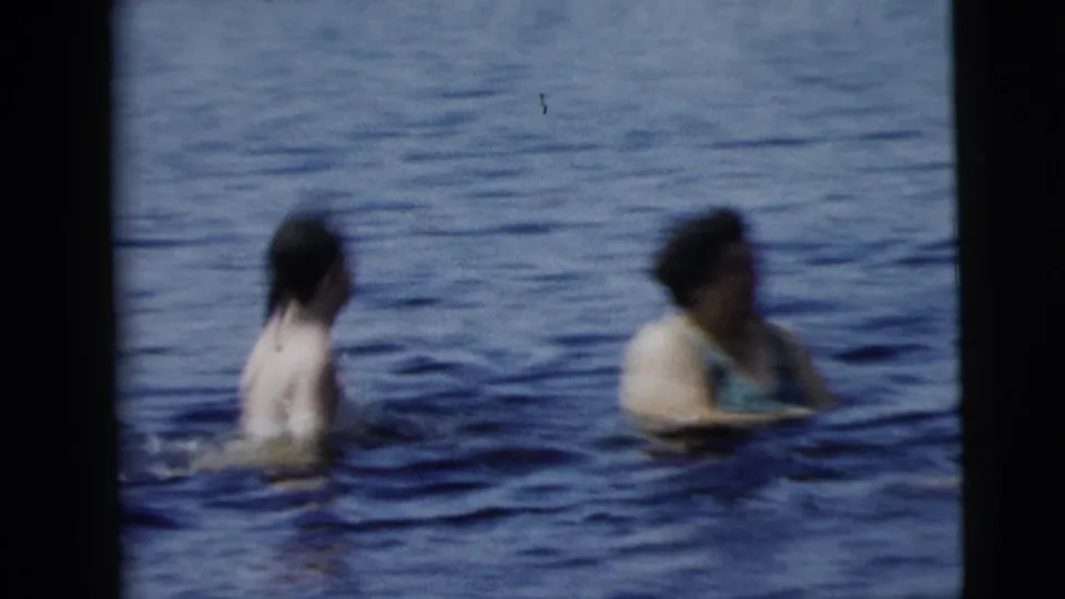 Camden, New Jersey home-movie frame showing two adults wading apart in open water, with soft focus and visible film texture.