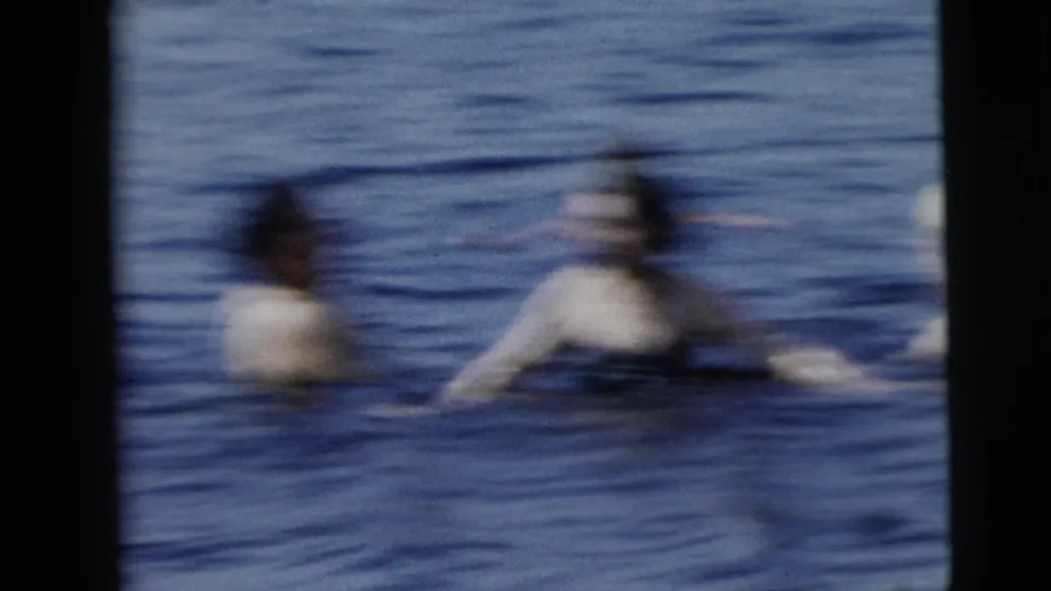 Soft, motion-blurred 8mm frame of adults playing or floating in open water during a 1962 swimming scene.
