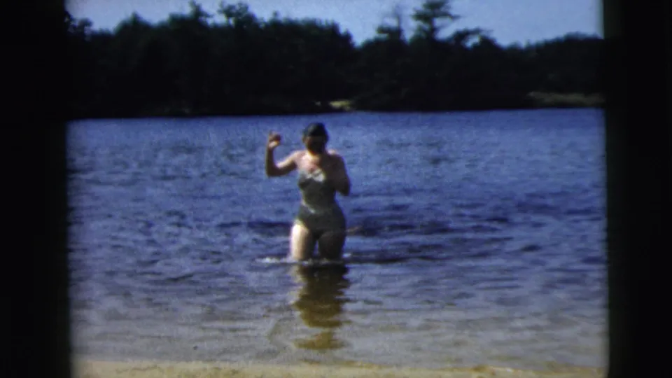 1962 8mm frame from Camden, New Jersey, with a woman waist-deep in lake water gesturing toward the home-movie camera.