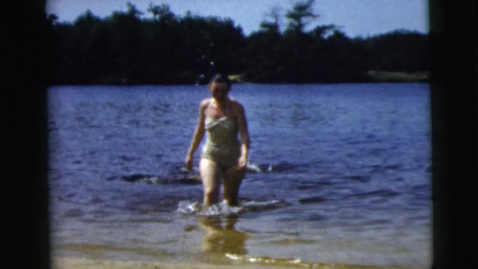 The woman continues walking through blue lake water in this supported 1962 Camden, New Jersey home-movie frame.
