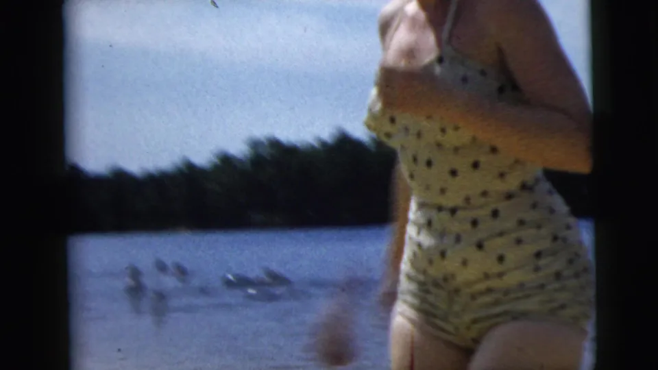Close 8mm view of the polka-dot swimsuit and torso as the woman moves past the camera at the lakeshore.