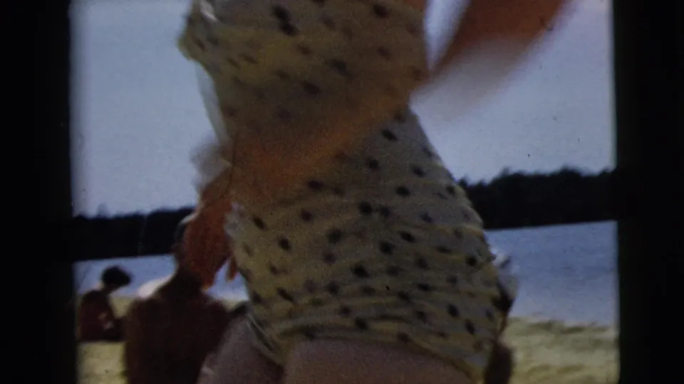 Close side view of the woman in a polka-dot swimsuit near the shore, with other swimmers seated by the lake.
