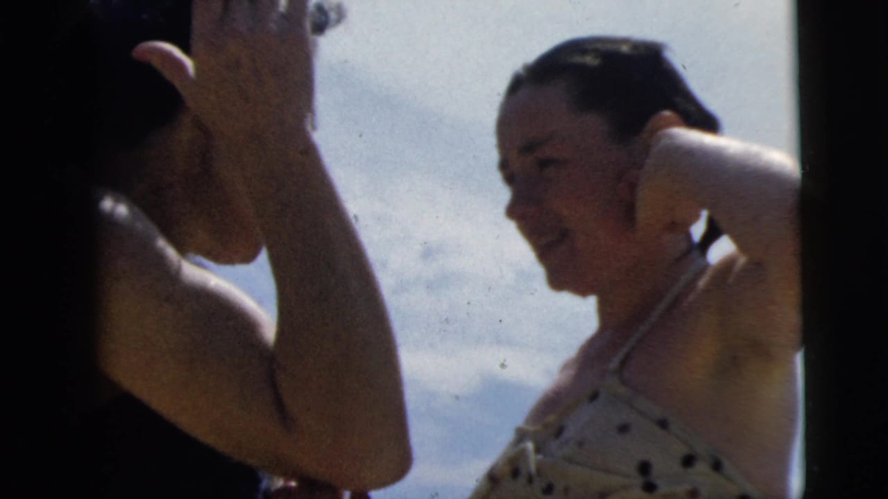 1962 Camden home-movie frame with two young women in bright sun, including one in a polka-dot swimsuit adjusting her hair.