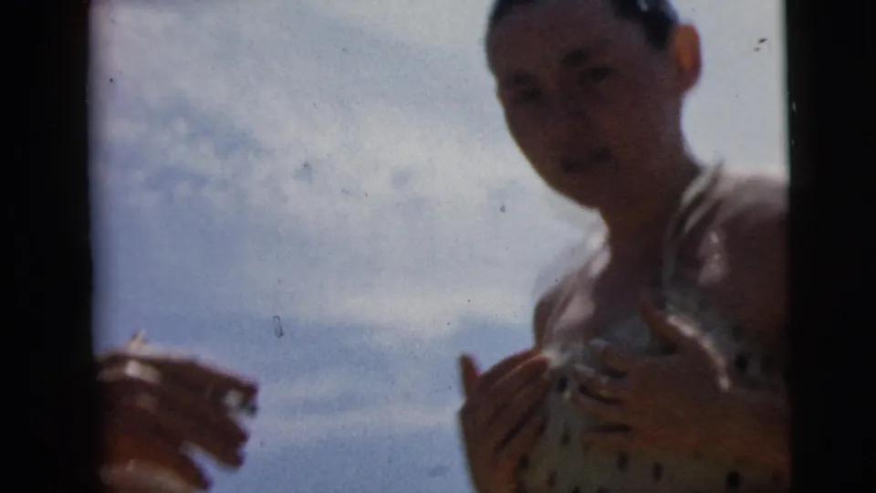 1962 Camden home-movie frame showing a young woman in a polka-dot swimsuit facing the camera under a bright sky.