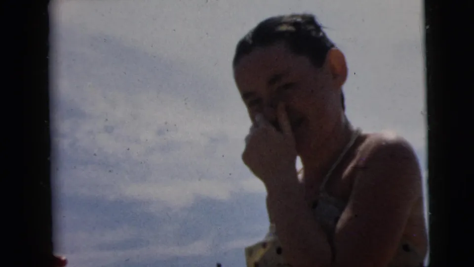 1962 Camden home-movie frame showing a young woman touching her face or eye in bright outdoor light.