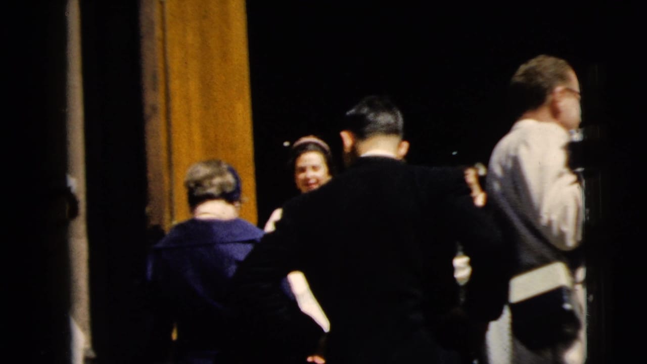 Adults gathered near a dark church entrance, with suits, dresses, and hats visible in sunlight.