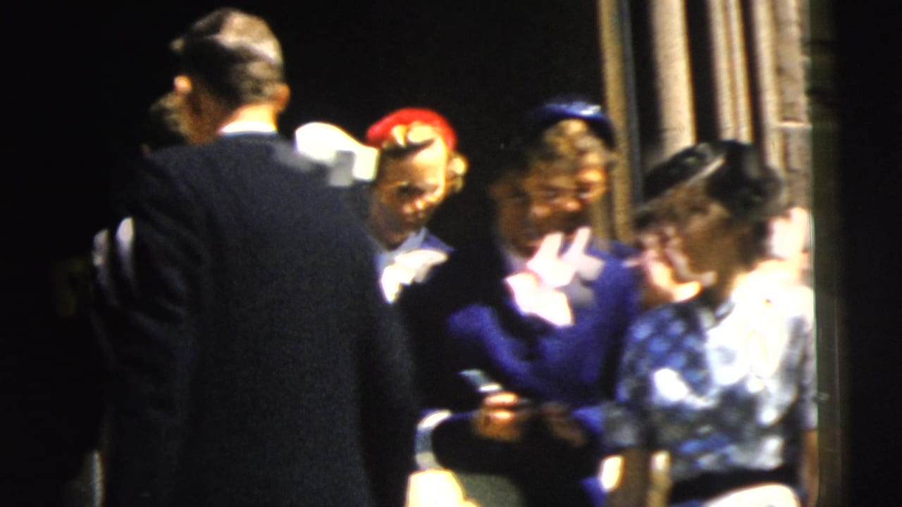 1962 Camden frame with churchgoers outside a stone building, including a prominent woman in blue beside other formally dressed adults.