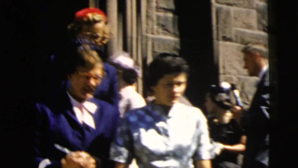 1962 Camden home-movie view of women in formal clothing moving past the church entrance as other adults gather nearby.