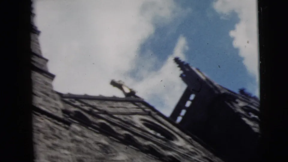 1962 Camden, New Jersey 8mm frame showing an angled stone roofline, dark window structure, and blue sky with scattered clouds.