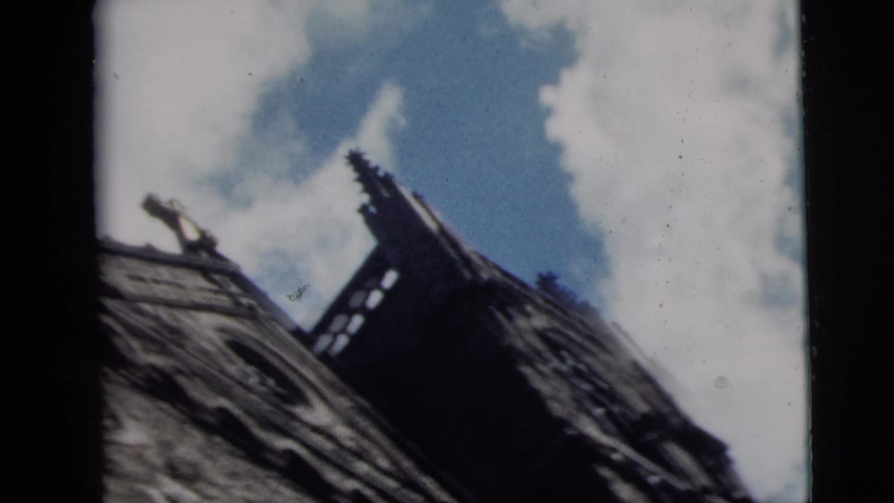 1962 Camden home-movie frame showing a low-angle church steeple or roofline against blue sky and white clouds.