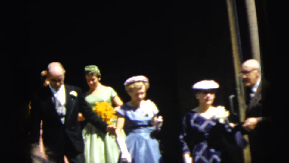 1962 Camden wedding party walks outside the church, with a man in a dark suit, women in dresses, hats, gloves, and flowers.