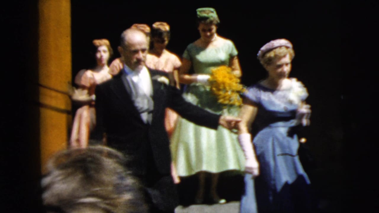 1962 Camden wedding home movie frame with a father in tuxedo escorting the bride in blue while pastel-dressed bridesmaids follow.
