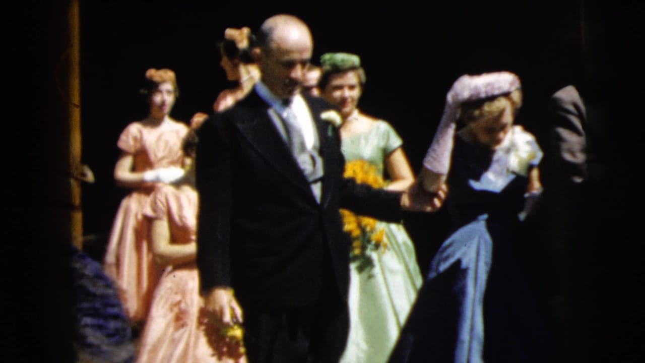Father walks beside the bride during a Camden, New Jersey wedding procession, with bridesmaids in green and pink dresses visible behind.