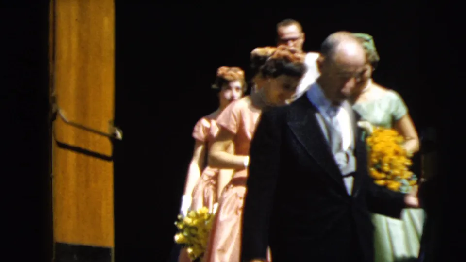 A late frame of the 1962 Camden wedding procession shows the father moving past the camera as pastel-dressed attendants carry flowers.